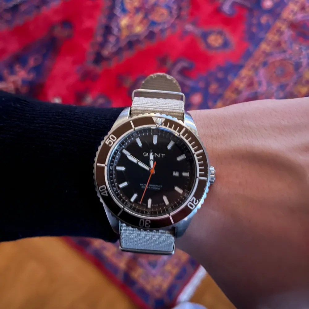 Snygg svart klocka från GANT med en stilren design. Den har en svart urtavla med vita markeringar och en grå textilarmband. Perfekt för den som gillar en klassisk och tidlös stil.. Asusteet.