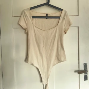 Beige bodysuit från H&M - Säljer en stilren beige bodysuit från H&M. Den har korta ärmar och en rundad halsringning. Perfekt för att matcha med jeans eller kjol för en enkel och snygg look.
