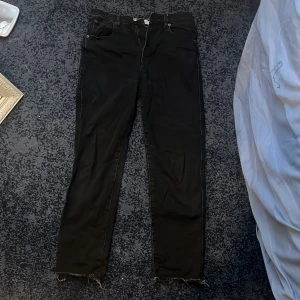 Svarta jeans  - Snygga svarta jeans med en klassisk femficksdesign och fransade kanter. Perfekta för en stilren look. De har en dragkedja och knapp framtill.