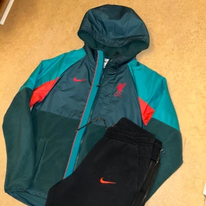 Nike Tech Fleece Tracksuit LFC (Sällsynt) - Säljer en snygg Limited Edition fleecejacka från Nike med dragkedja och huva. Jackan har ett stort Nike-märke på ryggen och LFC-logga på bröstet. Perfekt för en avslappnad stil. Lite damm på byxorna, inget smuts. Nypris 1700kr
