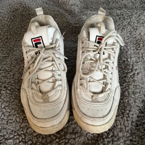 Vita sneakers från Fila - Snygga vita sneakers från Fila med klassisk design och snörning. Skorna har en robust sula och Fila-loggan på både tungan och hälen. Perfekta för en avslappnad stil.