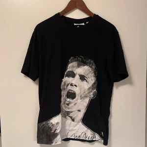 CR7 tröja  - Snygg svart t-shirt från Icons med ett stort porträtttryck i svartvitt på framsidan. Perfekt för dig som vill ha en unik och stilren look. T-shirten har en normal passform och är kortärmad.