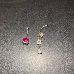 Två olika navelpiercingar - Säljer två jätte gulliga navelpiercingar utan kula. Den ena har en rosa sten i silverfärgad infattning, medan den andra har en hängande design med små blommor och klara stenar🩷