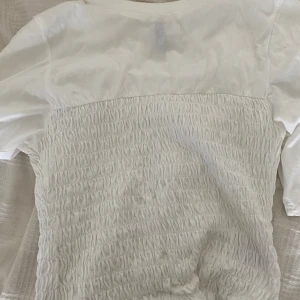 Vit topp med smockdetaljer - Säljer en vit topp med smockdetaljer på kroppen och korta ärmar. Säljer eftersom att den ej kommer till användning. Det är storlek M men funkar på mig som vanligtvis har storlek S.💓