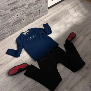 Mörkblå tröja från Ted Baker - Säljer en stilren mörkblå tröja från Ted Baker med deras logotyp tryckt på framsidan. Tröjan har långa ärmar och en klassisk rund halsringning. Perfekt för en avslappnad och snygg look.