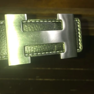 Svart skärp med silverfärgat spänne - Snyggt svart skärp med ett stort, silverfärgat spänne i metall. Perfekt för att ge en stilren touch till din outfit. Skärpet är gjort av skinn och har en klassisk design som passar till många olika stilar.