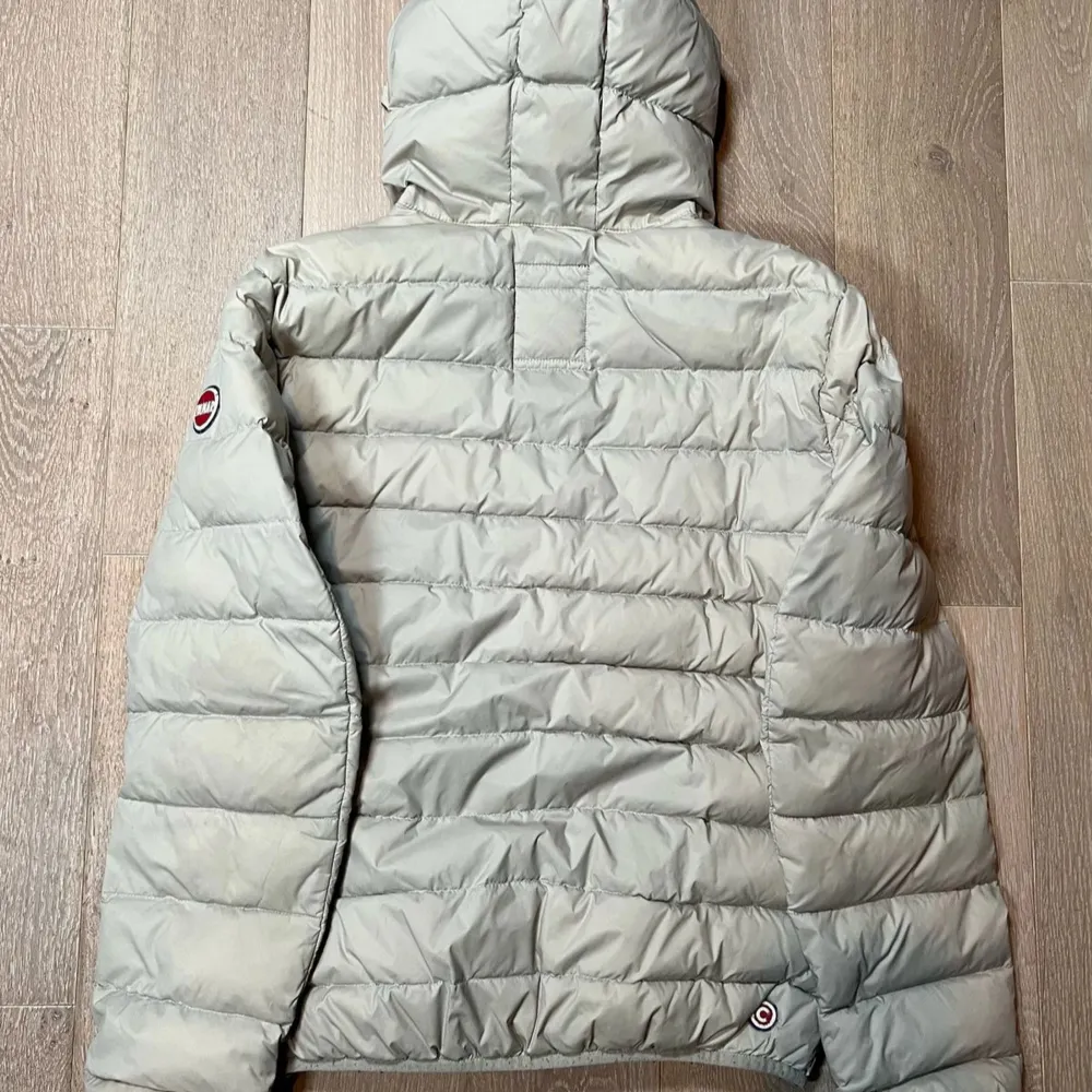 Snygg beige dunjacka från Colmar med huva och dragkedja. Jackan har en quiltad design och två praktiska fickor med dragkedja. Perfekt för kyligare dagar.. Takit.