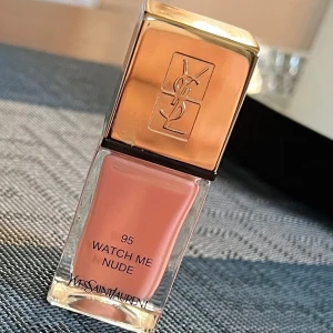 Yves Saint Laurent nagellack i nyansen Watch Me Nude - Nagellack från Yves Saint Laurent i nyansen 'Watch Me Nude'. Den har en mjuk, nude färg som passar perfekt för en fräsch och naturlig look. Förpackningen är lyxig med en guldig topp och den ikoniska YSL-loggan. Endast testad. 10 ml full storlek på flaskan 