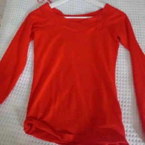 Röd långärmad topp - Snygg röd långärmad topp med en unik halsringning. Perfekt för att lysa upp garderoben med en stark färg. Passar bra till både jeans och kjol. Tröjan är röd/orange.