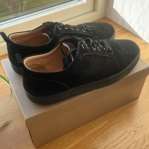 Svarta sneakers från Christian Louboutin - Snygga svarta sneakers i mocka från Christian Louboutin och kommer också med en lådan och påsen. Skorna smutsiga på sulan men syns inte så mycket längre. Några Knappar har börjat lossna vid snörena men går såklart fortfarande att knyta, kom med prisförslag