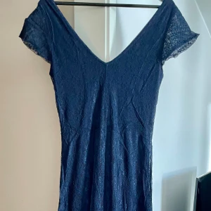 Marinblå spetsklänning vi från Soaked in Luxury - Elegant marinblå klänning i spets från Soaked in Luxury. Den har en v-ringad design och korta ärmar, perfekt för en stilfull look. Klänningen är i ett vackert spetsmaterial som ger en lyxig känsla.