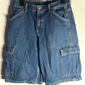 Mörkblåa jorts från H&M - Säljer ett par mörkblåa jorts från H&M med praktiska cargofickor på sidorna. Jortsen har justerbar midja och går ner över knäna.  
