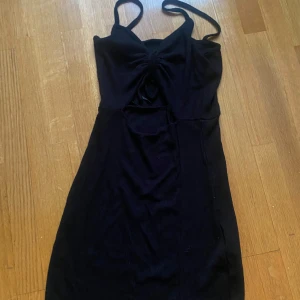 Svart klänning med knyt - Snygg svart klänning med knyt framtill och smala axelband. Perfekt för en kväll ute eller en speciell tillställning. Klänningen har en figurnära passform som framhäver silhuetten.