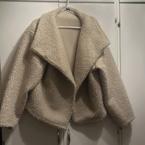 Beige teddyjacka - Mysig beige teddyjacka med stor krage och långa ärmar. Perfekt för kyliga dagar när du vill hålla dig varm och stilren. Jackan har en avslappnad passform och är lätt att matcha med olika outfits.