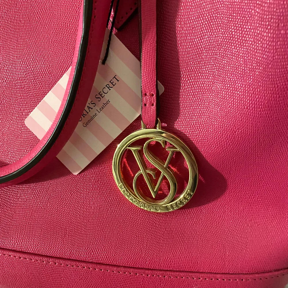 Snygg rosa handväska från Victoria's Secret med gulddetaljer och en praktisk dragkedja upptill. Väskan har två handtag och en dekorativ VS-logga i guld. Perfekt för att ge din outfit en färgklick! ÄR I ÄKTA LÄDER!!. Laukut & Käsilaukut.