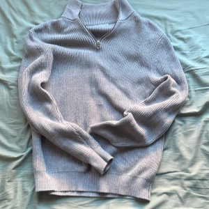 Grå stickad tröja från Zara - Säljer en stilren grå stickad tröja från Zara med dragkedja vid halsen. Tröjan har långa ärmar och ribbade muddar vid ärmslut och nederkant. Perfekt för kyligare dagar.