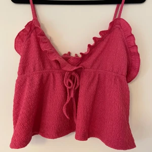 Rosa croppad linnetopp - Söt rosa croppad linnetopp med volangdetaljer och knytning framtill. Tunna axelband och en luftig passform.