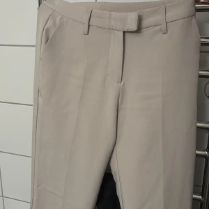 Beige kostymbyxor från BikBok - Snygga beige kostymbyxor från BikBok med en klassisk design. Byxorna har en rak passform och är tillverkade i ett mjukt material som ger en elegant look. Perfekta för en stilren outfit.