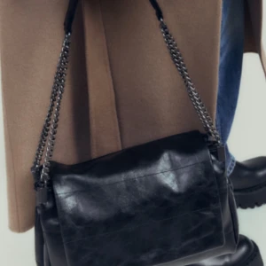 Svart axelväska med kedjedetaljer - Snygg svart axelväska i skinn med stiliga kedjedetaljer på axelremmen. Perfekt för att ge en edgy touch till din outfit. Väskan har en praktisk storlek för att bära med sig det nödvändigaste. Den är helt slutsåld på zaras hemsida, om ni har några funderingar elelr vill ha fler bilder är det bara att höra av sig💗 pris kan diskuteras 