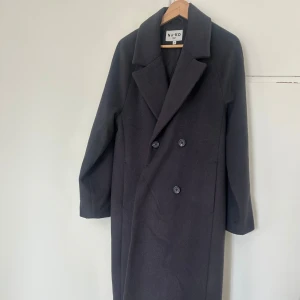 Svart kappa från NA-KD - Ny elegant svart kappa från NA-KD med klassisk design och knappar framtill. 