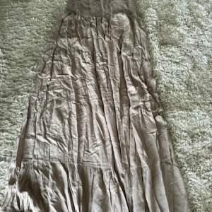 Beige långkjol/klänning  - Säljer en elegant beige långkjol/klänning med en smockad midja som ger en bekväm passform. Kjolen har ett vackert fall och är perfekt för både avslappnade och mer uppklädda tillfällen. Den neutrala färgen gör den lätt att matcha med olika toppar.