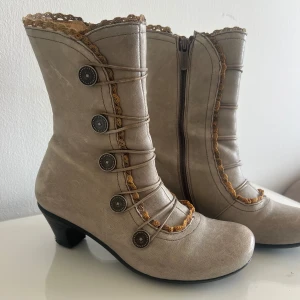 Beige boots med knappar från Brako - Snygga beige boots från Brako med dekorativa knappar och dragkedja på sidan. Skorna har en liten klack. Storlek 36, gott skick!