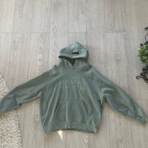 Grön hoodie från Essentials Fear of God - Säljer en stilren grön hoodie från Essentials Fear of God. Perfekt för en avslappnad stil. Precis som helt ny och knappt använd