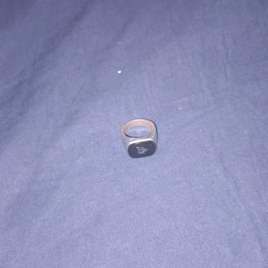 Svart ring med rektangulär platta - Cool ring med svart rektangulär platta och diskret mönster på ovansidan. Ringen har en stilren och modern design som passar perfekt för dig som gillar accessoarer med attityd.