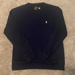 Mörkblå tröja från Polo Ralph Lauren - Säljer en klassisk mörkblå sweatshirt från Polo Ralph Lauren med den ikoniska vita loggan broderad på bröstet. Tröjan har rund halsringning och långa ärmar. Perfekt för en stilren och avslappnad look. Nyskick och storlek S.