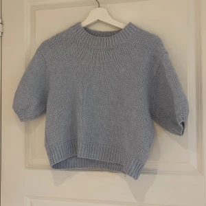 Ljusblå stickad tröja från Zara - Superfin ljusblå stickad tröja från Zara med korta ärmar och rund hals. Tröjan har en avslappnad passform och ribbade kanter vid hals, ärmslut och nederkant. Perfekt för lager-på-lager under kyliga dagar.