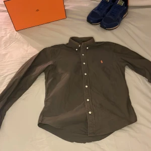  Ralph Lauren skjorta  - Säljer en olivgrön skjorta från Ralph Lauren i slim fit med klassisk krage och knappar framtill. Skjortan har lång ärm och den ikoniska broderade loggan i orange på bröstet. Perfekt för dig som gillar stilrena plagg med snygga detaljer. skjortan är i otroligt bra skick och är endast används någon enstaka gång då jag snabbt växte ur den. Jag tar gärna byten som vanligt. Priset är självklart diskuterarbart