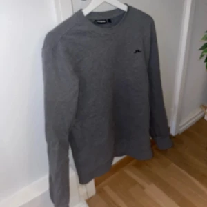 Grå sweatshirt från J.Lindeberg - En stilren grå sweatshirt från J.Lindeberg med rund halsringning och diskret logga på bröstet. Tröjan har långa ärmar och är tillverkad i mjukt material som passar perfekt till vardags.