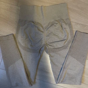 Beige träningsbyxor - Säljer ett par beigea träningsbyxor med hög midja och ribbade detaljer längs sidorna och midjan. Stretchigt material som sitter tight och formar sig efter kroppen. Det är Scrunch vid rumpan så att rumpan formas till en perfekt form. Perfekta för träning eller en chill dag.
