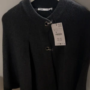 Mörkgrå poncho från Zara - Säljer en helt ny oanvänd poncho kappa från Zara, råka beställa fel storlek 🥰 och de har gått över tid så de går inte att lämna tbx den, den e asssnygg med kort kjol eller vanliga low waist bootcut jeans. 