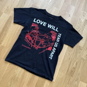 Svart t-shirt från Pleasures med tryck size M - Säljer en svart t-shirt från Pleasures med stort grafiskt tryck i rött och vitt framtill. Texten 'LOVE WILL TEAR US APART' och ett konstnärligt motiv ger en cool och edgy vibe. Klassisk passform och rund hals.