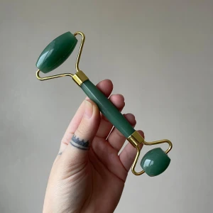 Grön ansiktsroller i jade från Cloud & Glow - Säljer en grön ansiktsroller i jade eller aventurin med gulddetaljer från Cloud & Glow. Rollern har två olika storlekar på stenarna för ansikte och ögonområde. Perfekt för att massera in serum eller ansiktsolja och ge huden extra lyster. Den är oanvänd men lådan har lite fläckar efter att ha legat bredvid någon i en låda.