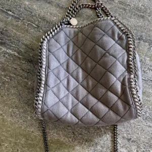 Grå quiltad axelväska från Stella McCartney -  Säljer en snygg grå fallabella axelväska från Stella McCartney med kedjedetaljer och quiltat mönster. Väskan har silverfärgad kedja som axelrem och endast defekt på en liten del av kedjan. Perfekt accessoar för att lyfta din outfit! Lånade bilder av hon jag köpte väskan av men bara att skriva för fler bilder 🥰