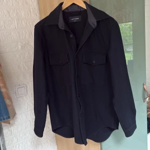 Overshirt från A Day's March - Säljer en mörkblå overshirt från A Day's March i storlek medium, den passar dock lite större. Skjortan har långa ärmar, två bröstfickor med knappar och klassisk krage. Perfekt att bära som lager över en t-shirt eller tröja.