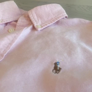 Rosa skjorta från ralph lauren✨ - 🌟 Rosa Stilig Skjorta från Ralph Lauren 🌟  Säljer en elegant Rosa skjorta från Ralph Lauren, perfekt för alla tillfällen! Den har bara använts ett fåtal gånger och är i mycket bra skick, utan några tydliga defekter. ✨  👕 Specifikationer: - Material: 100% bomull - Storlek: S (man) Dock är den köpt med specifikationen Small/petite  det menas att den är smalare än vanligt. Denna skjorta kombinerar stil och komfort, vilket gör den till ett utmärkt val för både festliga och vardagliga tillfällen😁