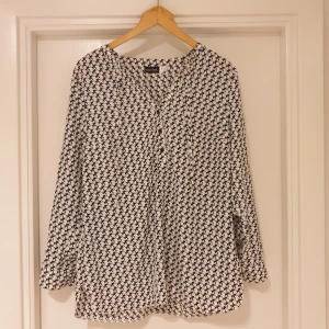 Svartvit blus med kattmönster från Laura Kent - Säljer en svartvit blus från Laura Kent med unikt kattmönster. Blusen har långa ärmar, knappar framtill och en lös passform. Perfekt för dig som gillar roliga detaljer och vill sticka ut lite extra.