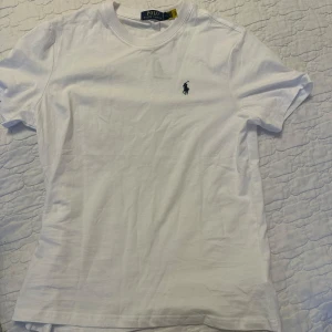 Vit t-shirt från Polo Ralph Lauren - Klassisk vit t-shirt från Polo Ralph Lauren med liten broderad logga på bröstet. T-shirten har rund halsringning och korta ärmar. Perfekt basic-plagg med snygg passform och mjukt bomullsmaterial. Har fortfarande taggen och allting på. Fick den som present men den kom aldrig till användning. Jag kan förhandla om pris!