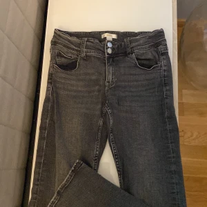 Mörkgrå jeansbyxor från Gina Tricot - Säljer ett par svarta jeansbyxor från Gina Tricot med klassisk femficksdesign och silverfärgade knappar. Jeansen har normal passform och raka ben, perfekta till vardags. Tidlös modell som passar till det mesta.