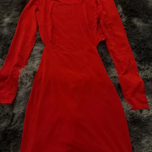 Röd långärmad klänning med rynkdetalj - Säljer en snygg röd klänning med långa ärmar och rynkdetalj framtill. Klänningen har en figurnära passform och är perfekt för dig som vill sticka ut. Materialet känns mjukt och följsamt.