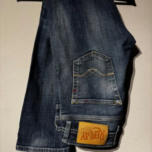 Replay jeans - Säljer ett par klassiska blå jeans från Replay med snygga slitningar och raka ben. Jeansen har fem fickor, gylf med dragkedja och tydlig Replay-lapp bak. Perfekta för dig som gillar en tidlös look.