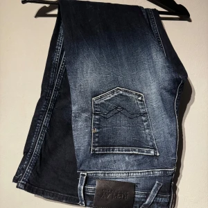 Replay jeans - Säljer ett par mörkblå jeansbyxor från replay med slitningar och snyggt tvättad look. Byxorna har raka ben, klassiska fem fickor och normal passform. Perfekta för dig som gillar en lite ruffare stil.