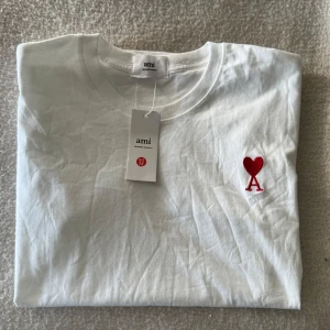 Vit t-shirt från Ami Paris med ett rött hjärta - Säljer min Ami Paris T-shirt jag fick i födelsedagspresent, säljes pga att den är för liten i storlek för mig. Är storlek: S men passar även bra till M
