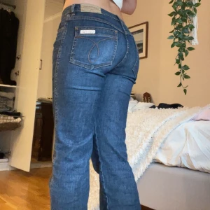 Blå jeansbyxor från Calvin Klein - Säljer ett par fina blå bootcut jeansbyxor från Calvin Klein. Byxorna har fem fickor, synliga sömmar och logotyp på bakfickan samt läderpatch i midjan. Jag skulle säga att de ligger i storlek mellan 36 och 38.