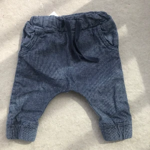 Blå småmönstrade byxor med dragsko - Säljer ett par blå byxor med små vita prickar och mjuk resår i midjan samt dragsko. Byxorna har uppvikta benslut och är perfekta för en avslappnad stil. Materialet känns mjukt och bekvämt.