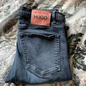 Mörkblå jeans från Hugo Boss - Säljer ett par mörkblå jeans från Hugo Boss med klassisk femficksdesign och rakt snitt. Jeansen har en tydlig Hugo-lapp bak i midjan och är tillverkade i ett mjukt denimtyg. Perfekta för dig som gillar stilrena och tidlösa jeans.