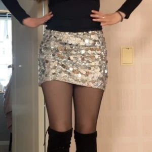 Silver paljettkjol  - Säljer en glittrig silverfärgad minikjol täckt med stora paljetter som ger en riktigt festlig look. Kjolen är kort och har en tight passform.